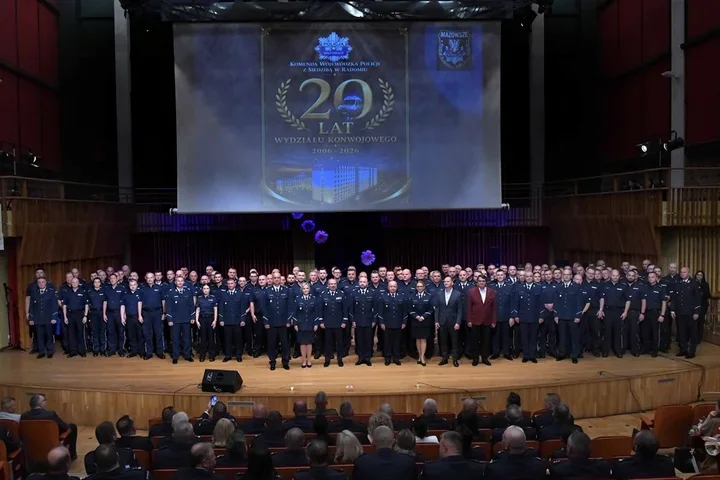 Grupa funkcjonariuszy policji i gości pozuje do pamiątkowego zdjęcia na scenie podczas uroczystości 20-lecia Wydziału Konwojowego Komendy Wojewódzkiej Policji w