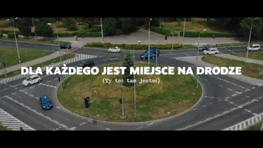 Widok z góry na rondo z przejeżdżającymi samochodami i naniesionym hasłem o bezpieczeństwie na drodze.