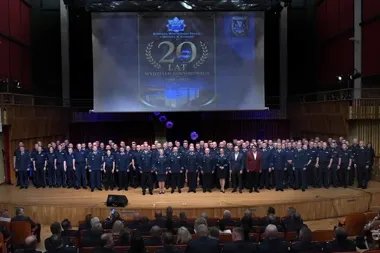 Grupa funkcjonariuszy policji i gości pozuje do pamiątkowego zdjęcia na scenie podczas uroczystości 20-lecia Wydziału Konwojowego Komendy Wojewódzkiej Policji w
